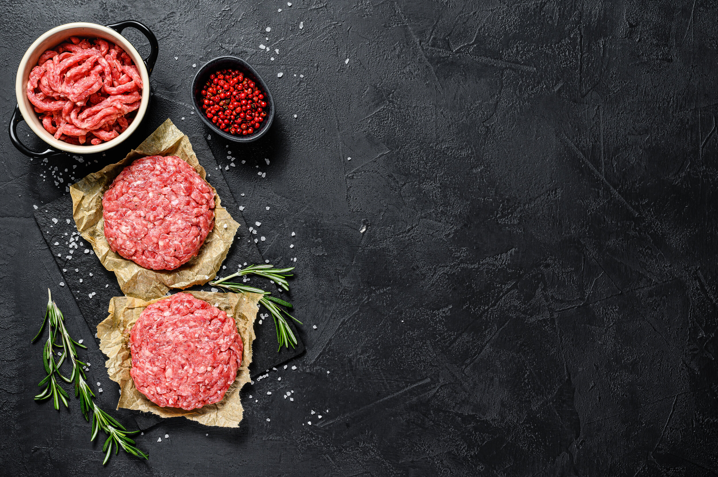 Ground raw meat patties. Meat patties ready to cook. Barbecue party. Farm organic meat. Black background. Top view. Space for text